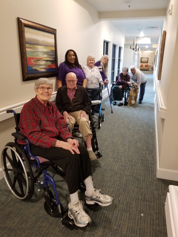A row of smiling residents using mobility aids in a hallway.