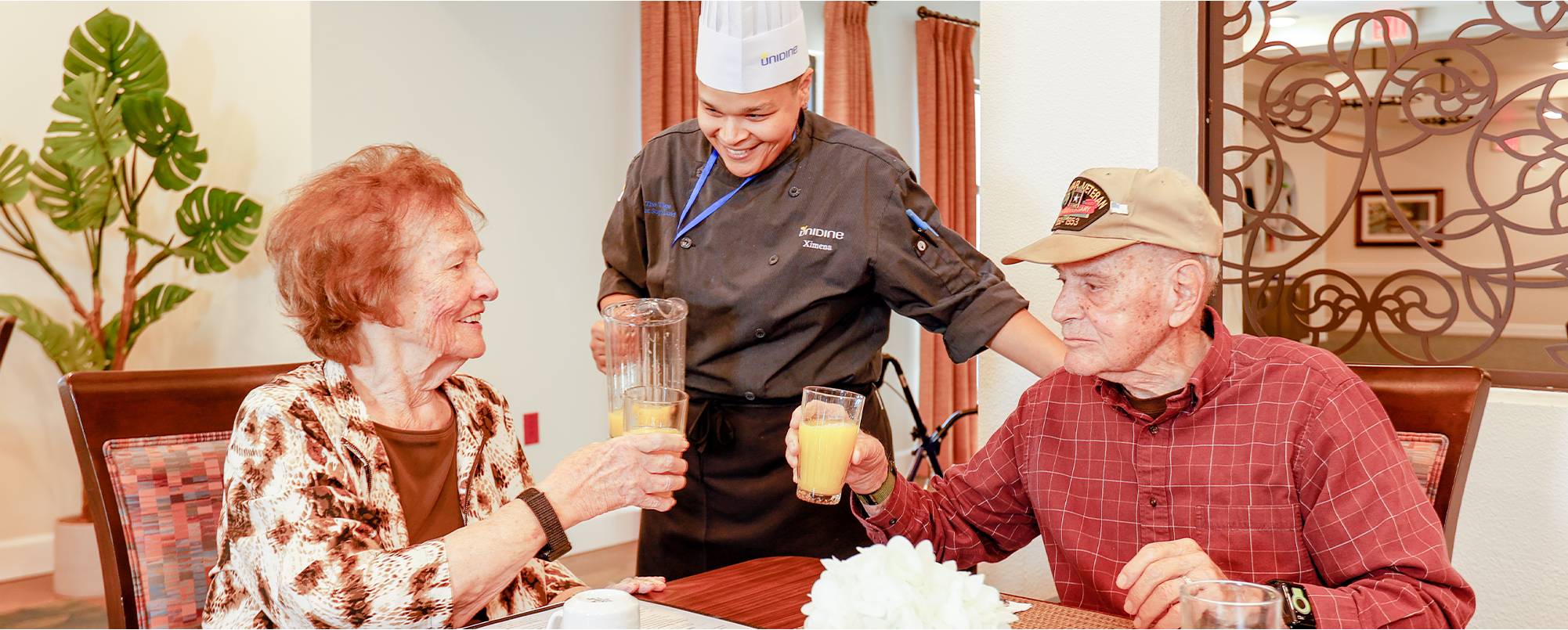A chef is serving two people drinks at the table.