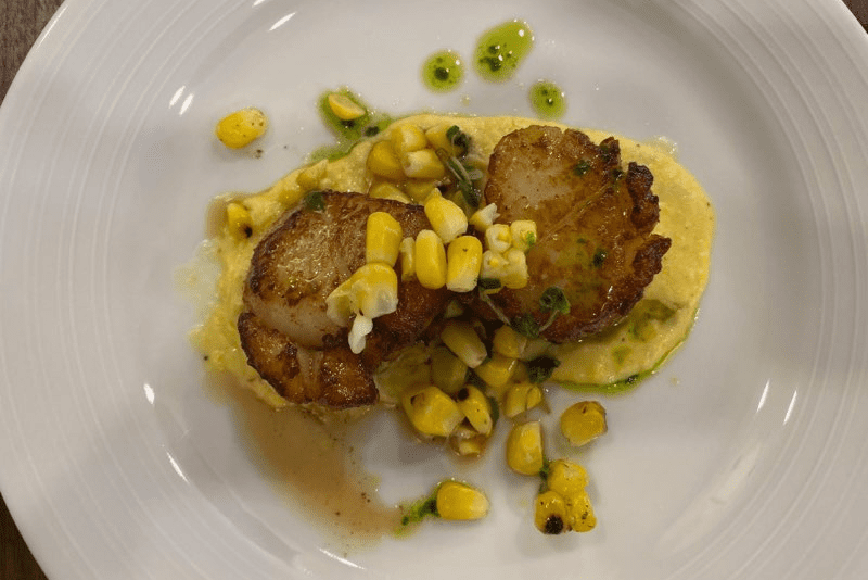 A plate of food with scallops and corn on it.