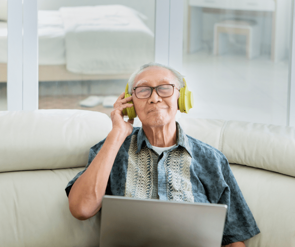 An older man wearing headphones while sitting on a couch.