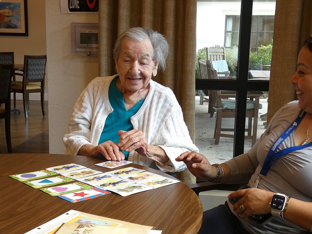 An elderly woman in end stage Alzheimer’s disease playing a card game with a caregiver at The Village at Sugar Land.