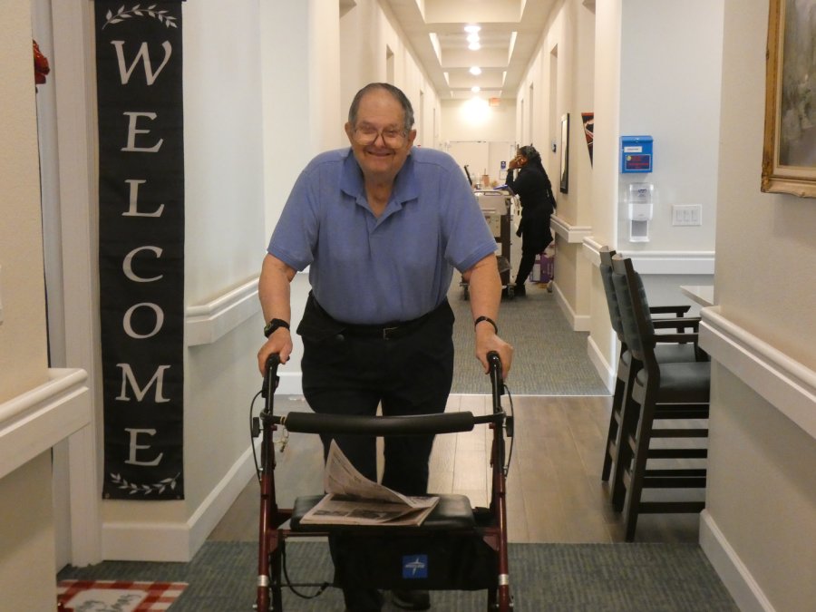 A resident walks down the hallways using a walker to support his gait.