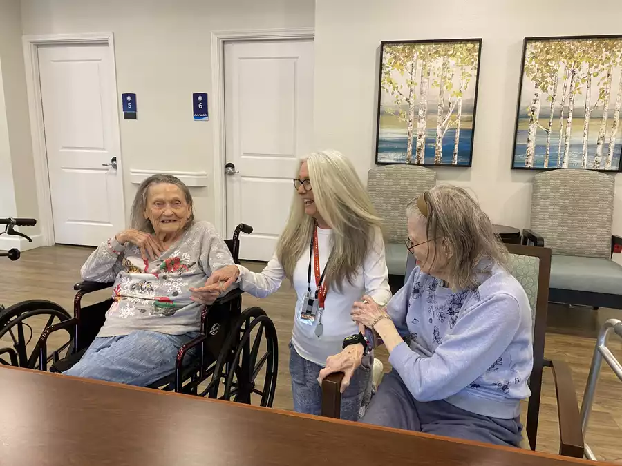 Two elderly women and a caretaker smiling and laughing