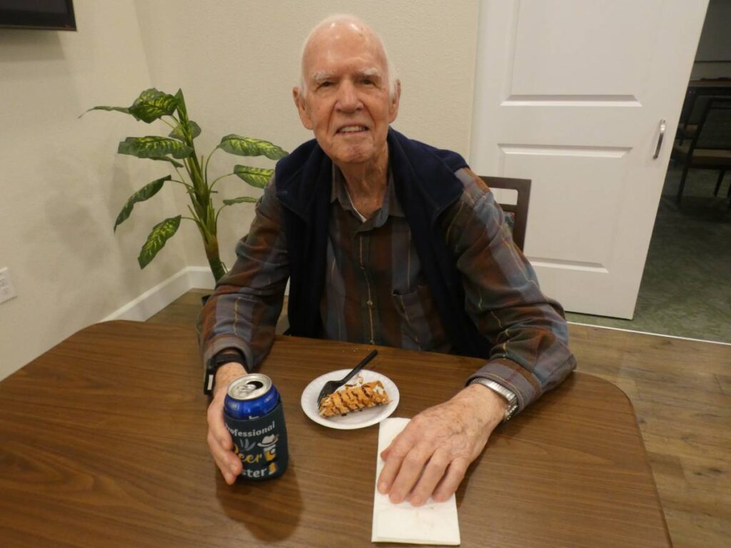 A happy elderly man have a drink and dessert at a table.