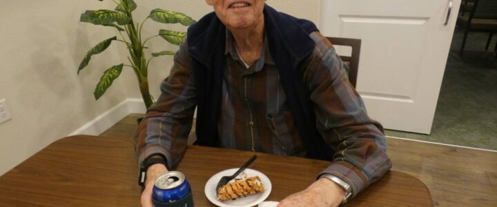 A happy elderly man have a drink and dessert at a table.